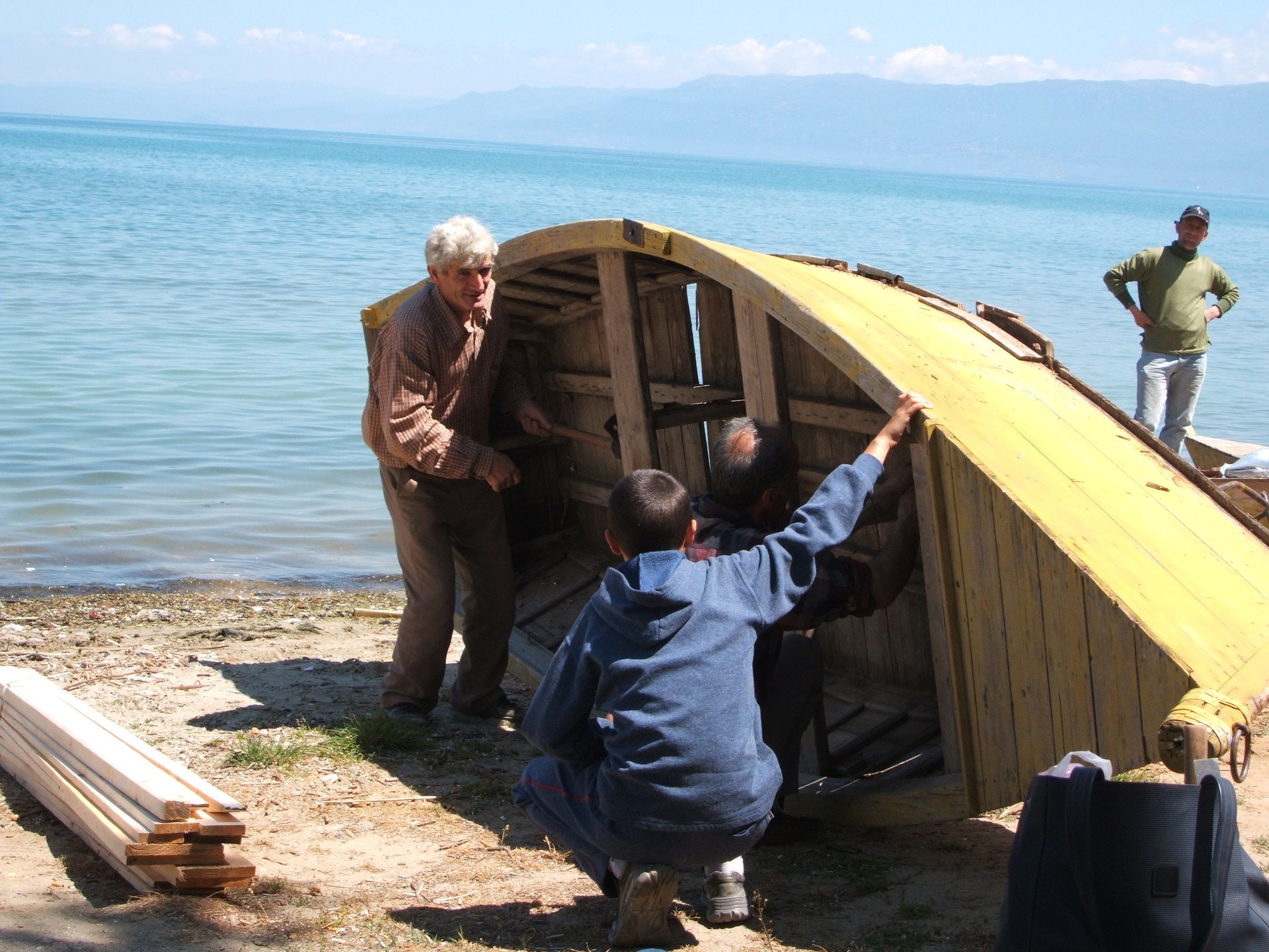 Community members restoring a traditional wooden boat by the lake